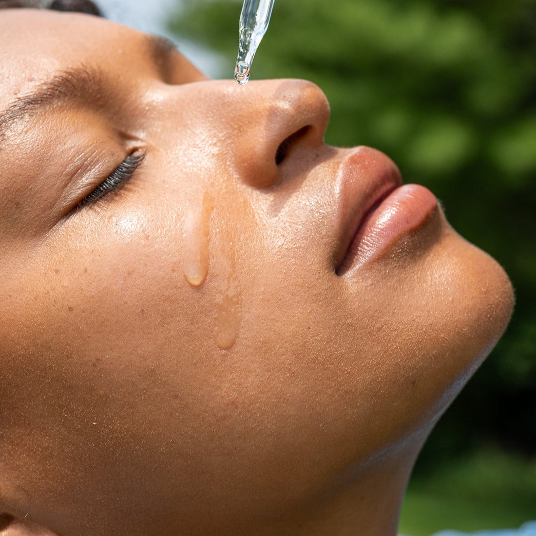 Person applying a dropper of face oil to their face outdoors