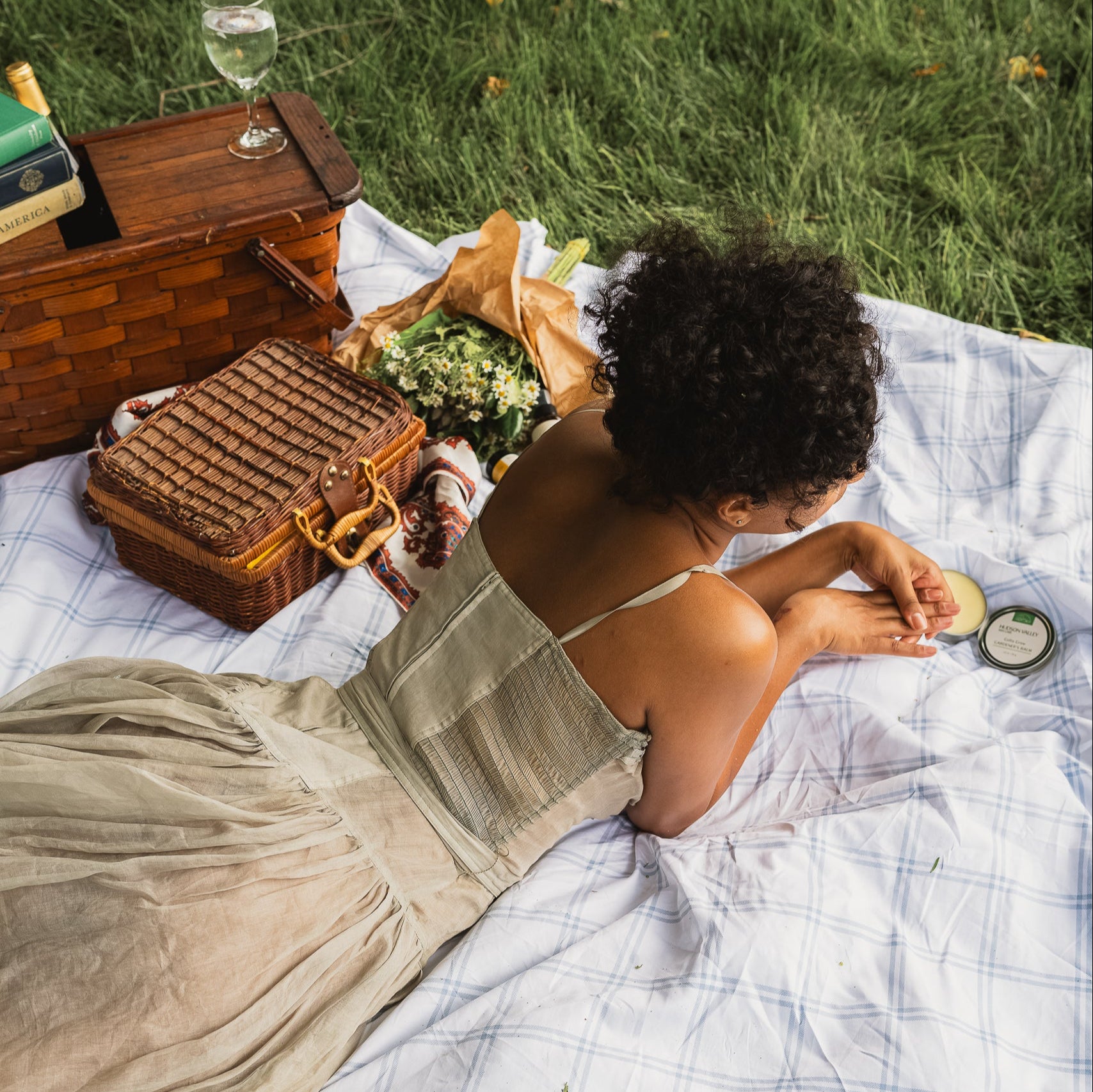 Woman relaxing on a picnic blanket with a basket and drinks in a park